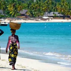 Trzy kobiety niosą kosze na głowach na plaży. Tropikalne palmy i budynki w tle. Idealne wakacje na Madagaskarze.