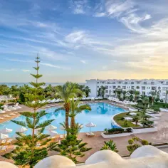 Hotel Palm Azur Djerba: rozległy basen, białe budynki, palmy i morze pod błękitnym niebem. Idealne miejsce na wakacje.