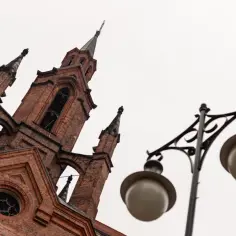 Gotycka wieża kościoła w Kalinicu, z cegły, z ozdobną latarnią uliczną na pierwszym planie.