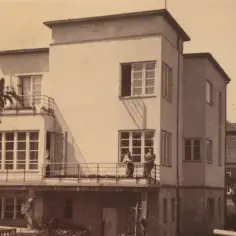 Dwaj mężczyźni stoją na tarasie modernistycznej willi w Grabówku. W tle widać inne budynki i drzewa.