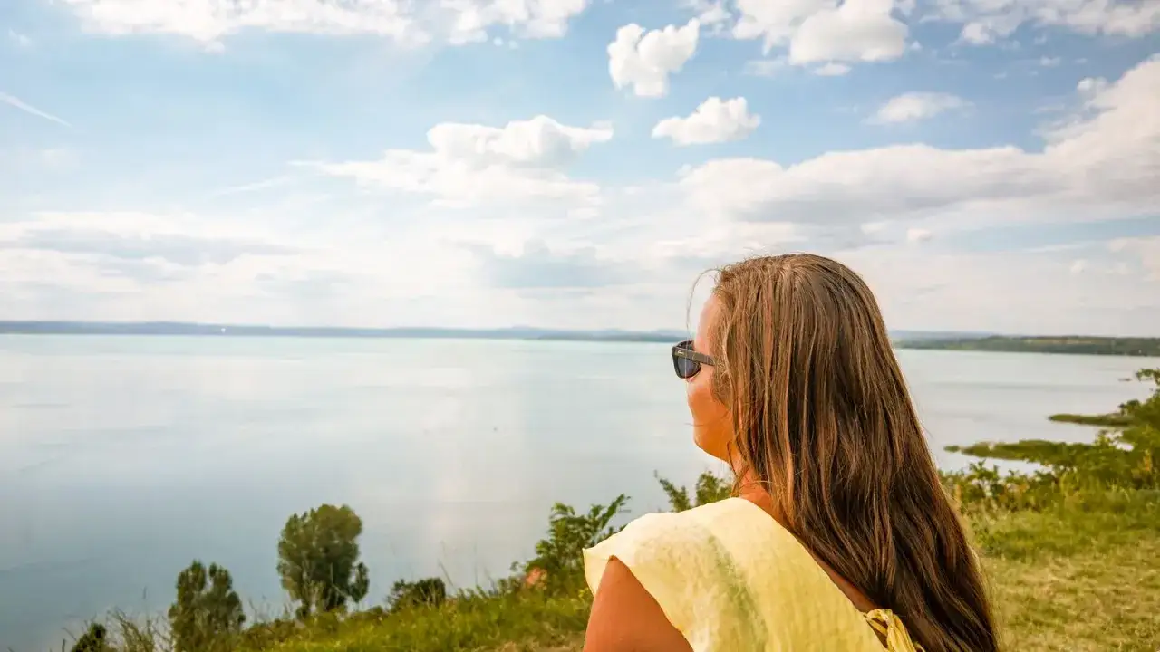 Kobieta w żółtej bluzce podziwia widok na Balaton. Idealne miejsce na wczasy nad Balatonem.