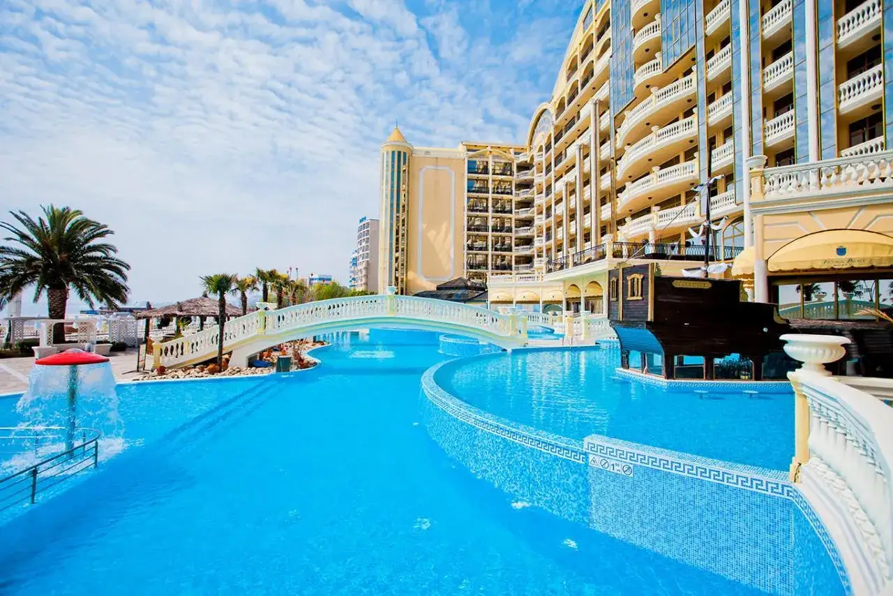 Luksusowy basen z mostkiem i palmami przy Imperial Palace Hotel.
