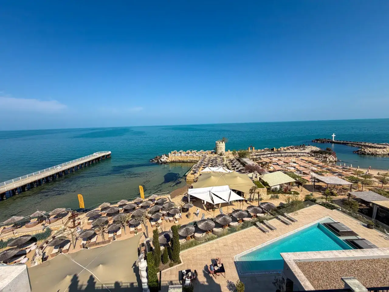 Widok na plażę z leżakami i parasolami, basen i morze. Idealne miejsce na wakacje w hotelu Nobel.
