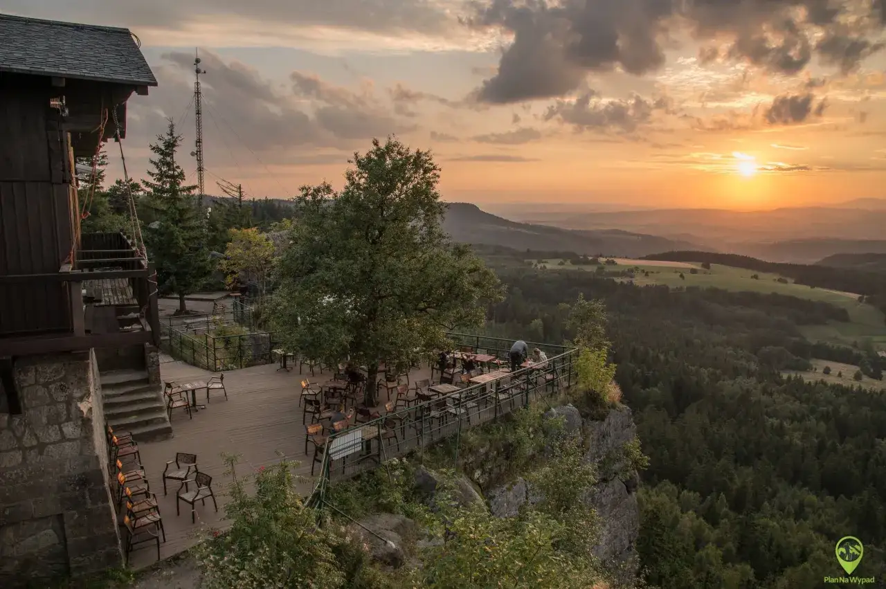Widok z tarasu restauracji na skalnym urwisku, gdzie są Sudety. Zachodzące słońce nad lasami i pagórkami.