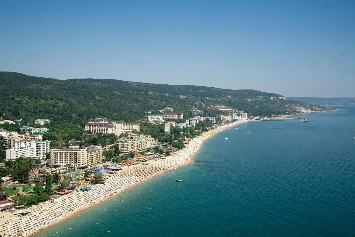 Słoneczny złoty brzeg Bułgaria tętni życiem. Hotele, plaża pełna leżaków i turystów, a w oddali zielone wzgórza.