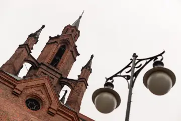 Gotycka wieża kościoła w Kalinicu, z cegły, z ozdobną latarnią uliczną na pierwszym planie.