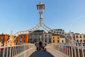 Most ludzi na moście Ha'penny w Dublinie, gdzie leży stolica Irlandii. Słońce zachodzi, oświetlając kolorowe budynki.