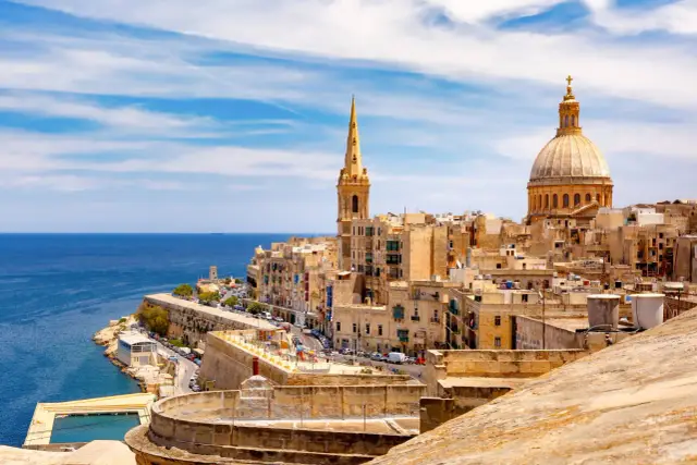 Malta last minute tanio! Widok na zabytkowe miasto z kopułą i wieżą, błękitne morze i basen. Idealne miejsce na wakacje.