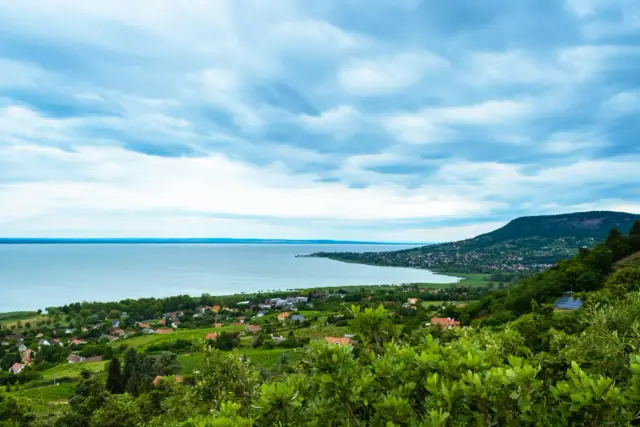 Malowniczy widok na Balaton, idealne miejsce na wczasy. W oddali widać wzgórza i zabudowania.