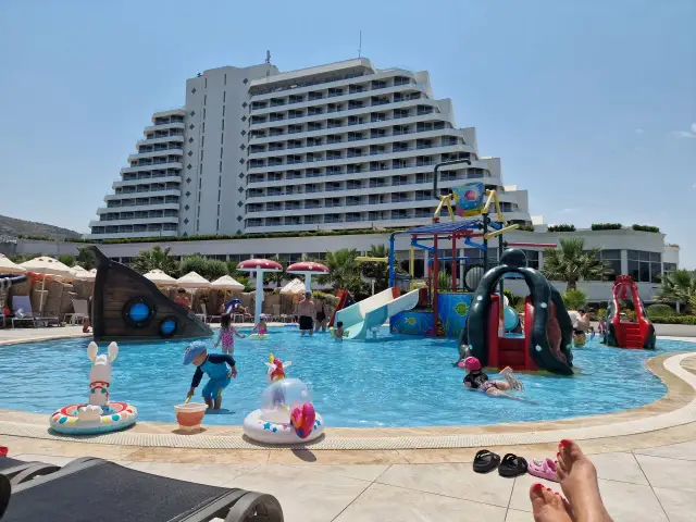 Basen z atrakcjami wodnymi dla dzieci przy hotelu Palm Wings Ephesus. Słoneczny dzień, woda, zjeżdżalnie i dmuchane zabawki.